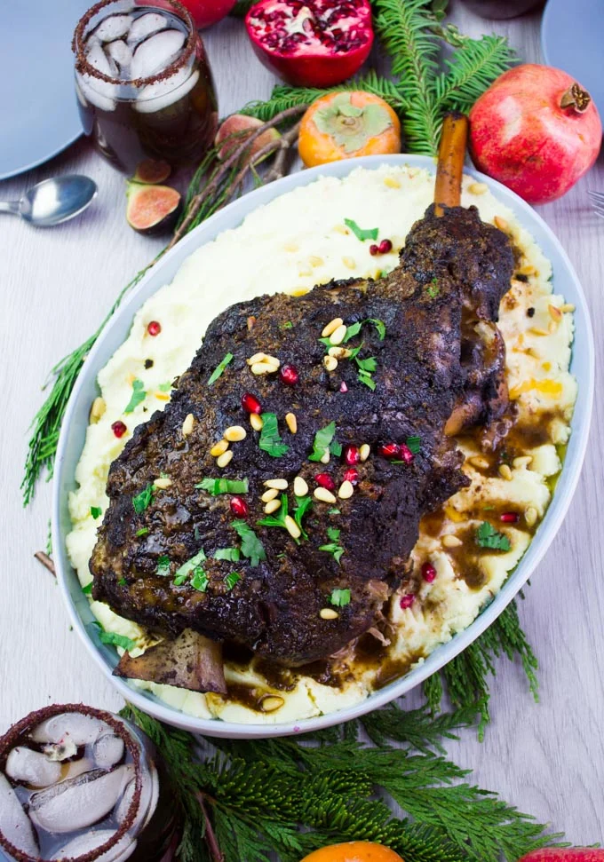 Close up of a plate showing the whole leg of lamb over mashed potatoes on a big plate , topped with parsley and pomegranate