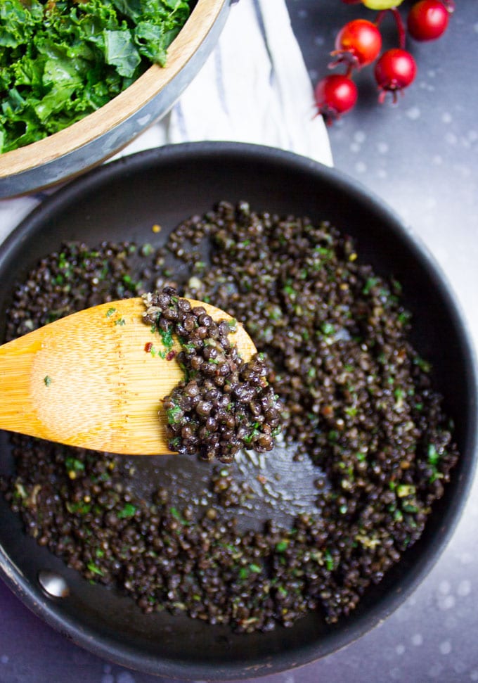 A wooden spoon showing the cooked spicy lentils ready with garlic and herbs