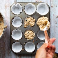 A hand filling in the muffin tin with the batter