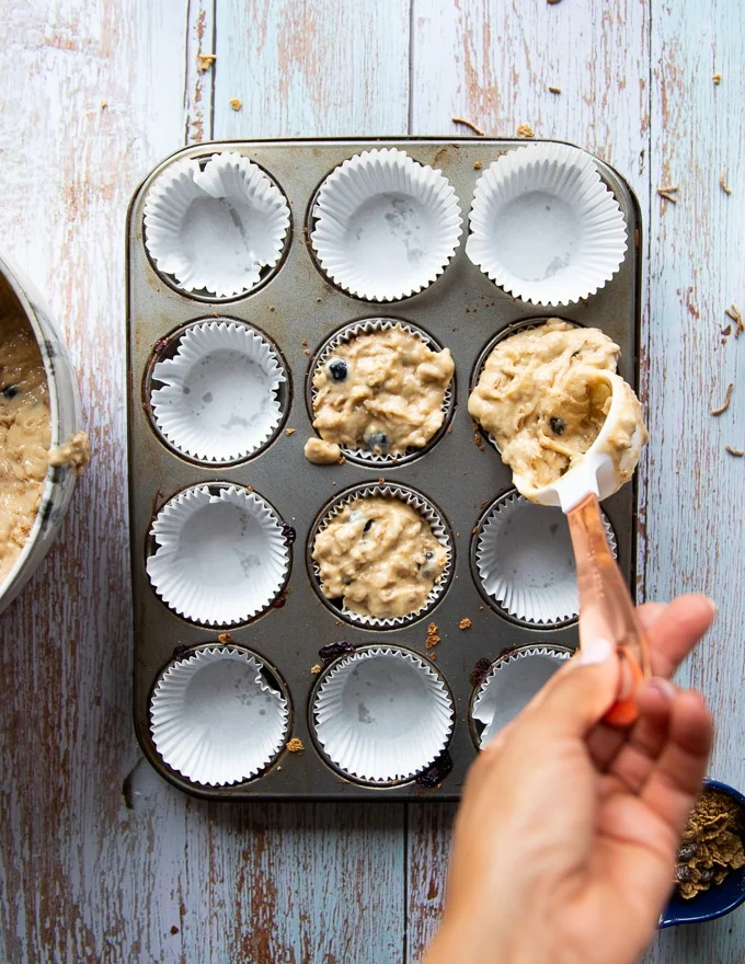 A hand filling in the muffin tin with the batter