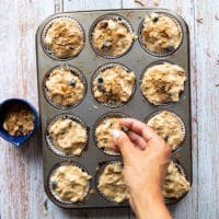 A hand sprinkling extra bran over the muffins before baking