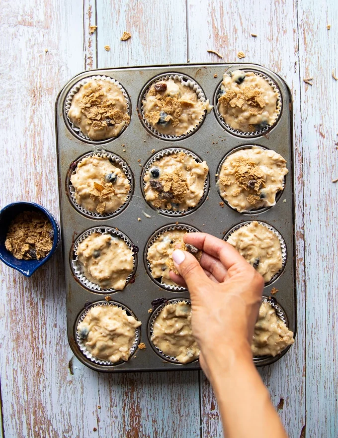 A hand sprinkling extra bran over the muffins before baking