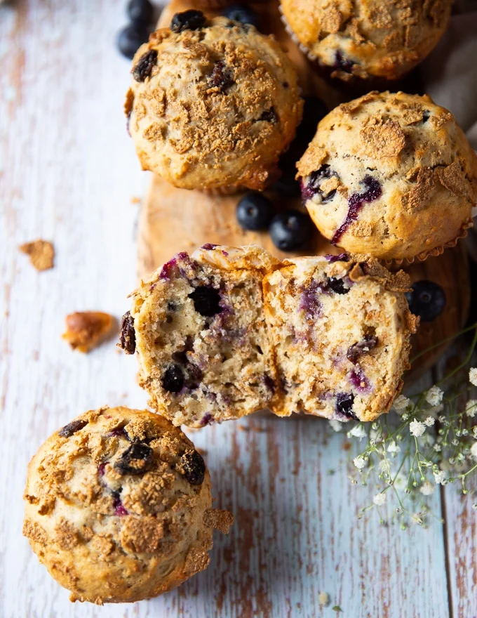 A bran muffin cut in half on a wooden board close to other bran muffins