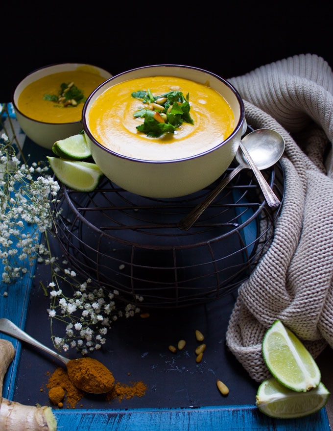 Two bowls of vegan butternut squash soups over a board and stopped with chopped parsleya nd pine nuts.