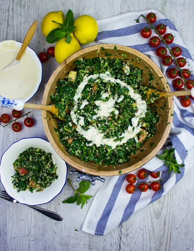Finished tabouli salad with two serving spoons and a small plate of salad on the side