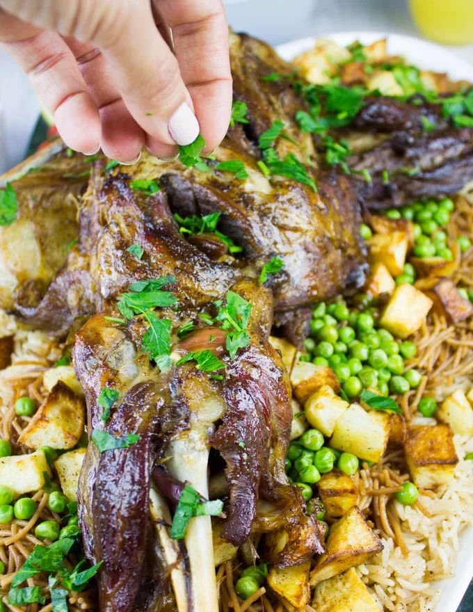 A hand sprinkling chopped parsley over the roast lamb shoulder