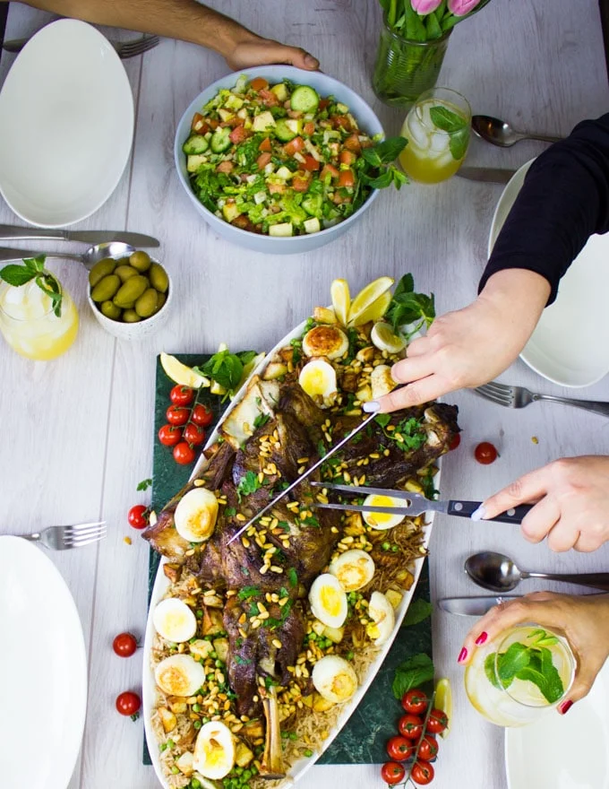 A table set up with the lamb shoulder recipe and a hand cutting through the lamb