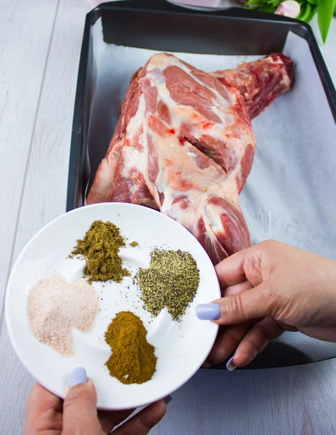 A hand holding the dry spice blend to sprinkle over the lamb shoulder