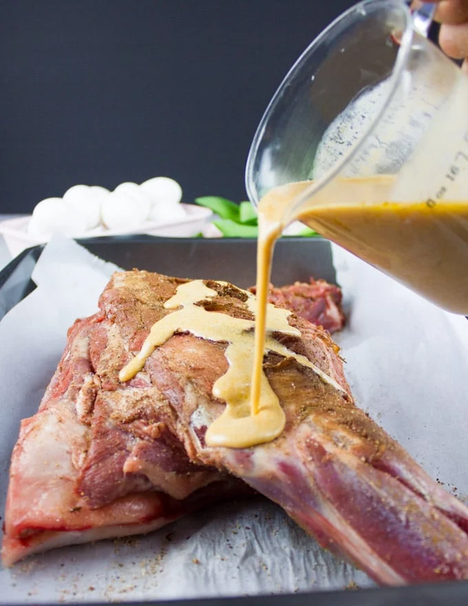 A hand pouring a wet marinade over the lamb shoulder
