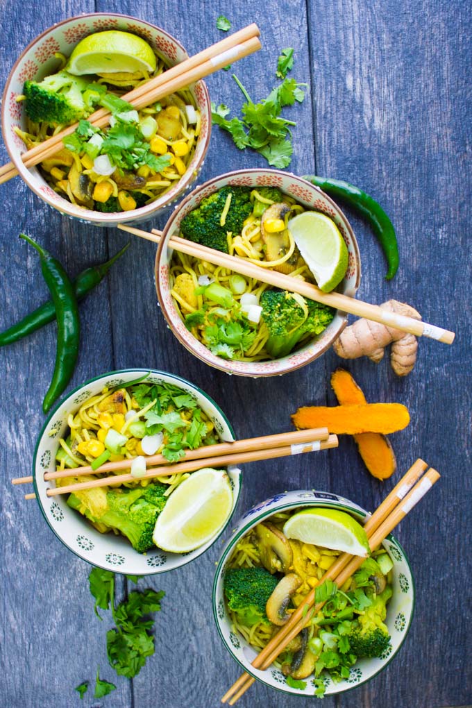 A set of 4 spicy ramn bowls with chopsticks and green chillies, lime wedges and turmeric root around it.