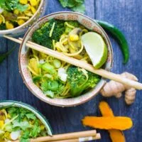 A bowl of spicy ramen with chopsticks for eating it, and turmeric root cut up with chillies around it.