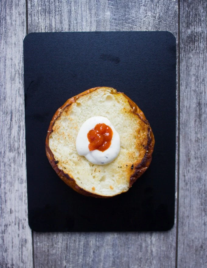 burgers buns spread with ranch and sriracha sauce ready to assemble the cheeseburger