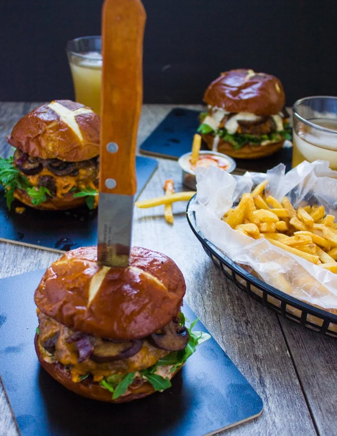 Cheese stuffed burger in a pretzel bun with a knife in the middle to slice it in half