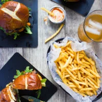 Cheese stuffed burgers on a table with one cheeseburger cut in half and some fries around it.