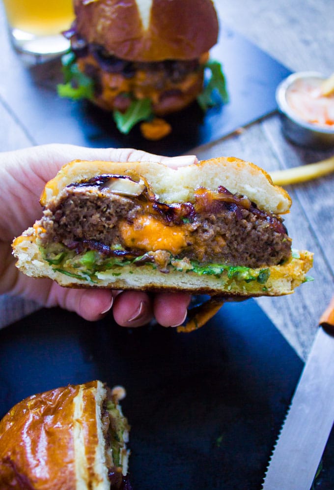 A hand holding a cheese stuffed burger cut in half showing the cheese center of the cheeseburger.