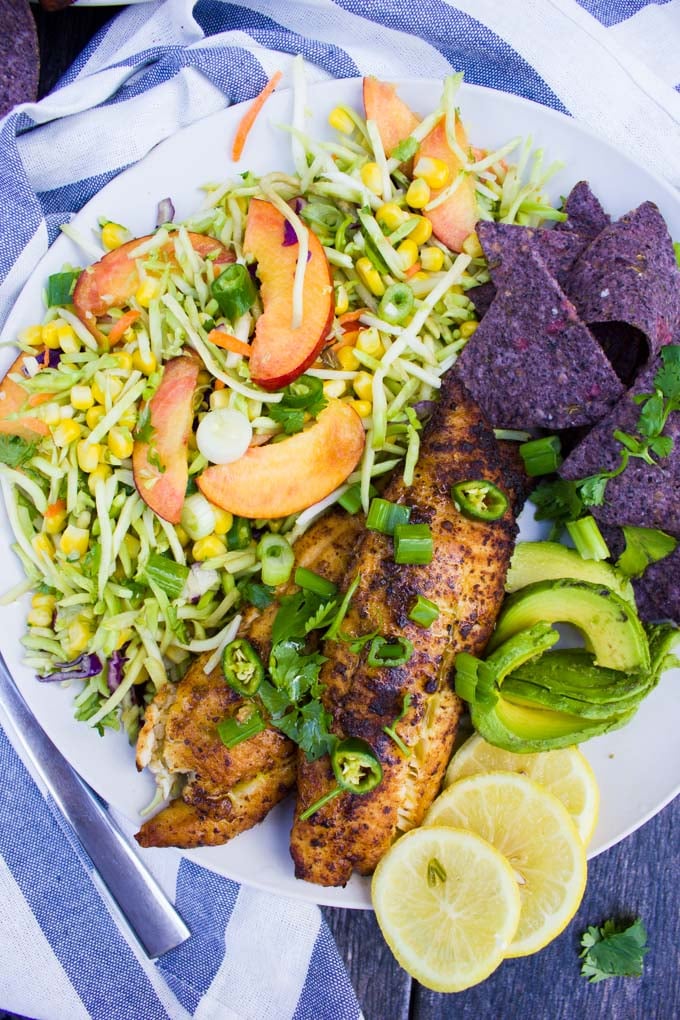 A close up of the fish taco recipe showing the taco slaw with peaches, a sliced avocado and lemon slices
