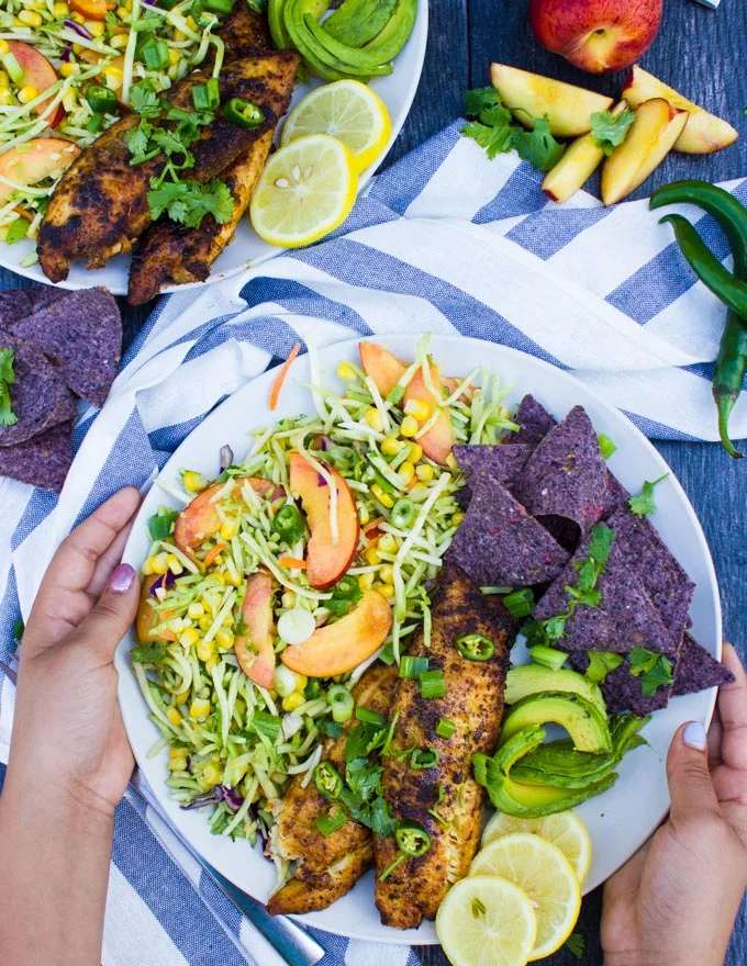 two hands holding a plate of fish taco recipe with taco slaw and chips