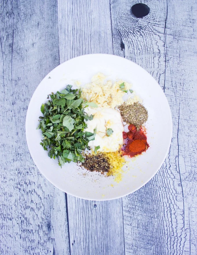 A plate of marinade ingredients for lemon chicken including mayo, lemon zest, herbs, garlic, spice
