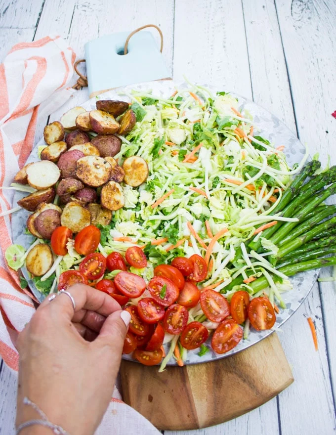 A hand assembling the salad adding tomatoes, grilled asparagus