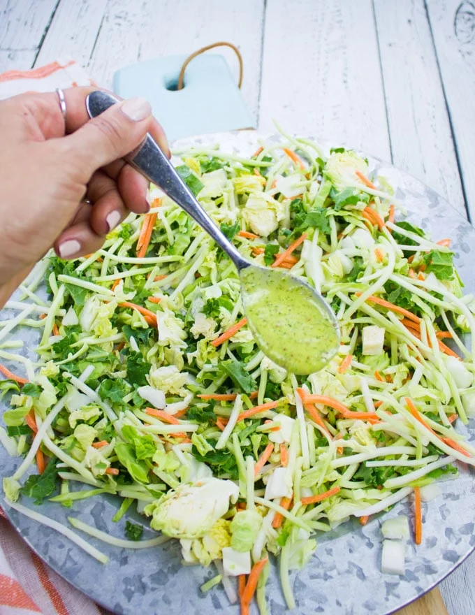 A hand drizzling some sweet dill dressing over the slaw mix