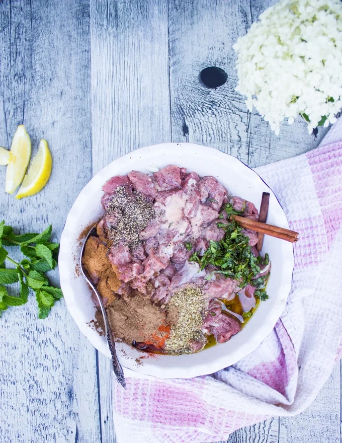 A bowl with lamb chunks and the spices on top, lemon slices and fresh mint