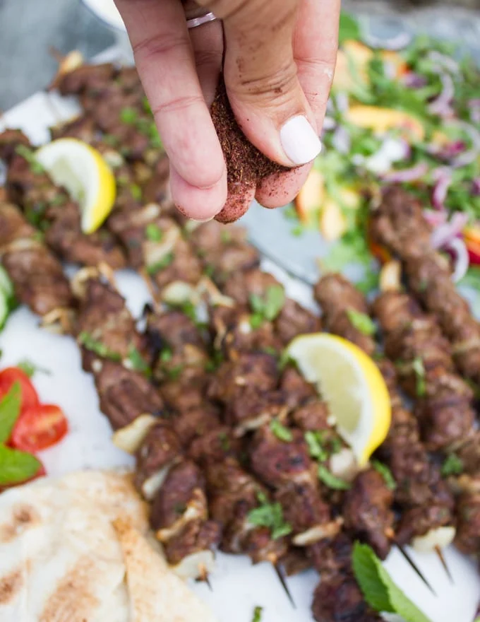 hand sprinkling sumac over the grilled lamb