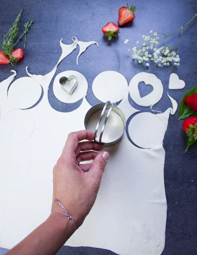 A hand holding a cookie cutter and cutting out rounds of puff pastry for the crust