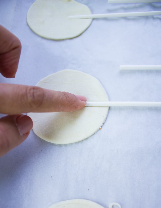 A hand pressing the lollipop stick at the center of the bottom crust of hand pies