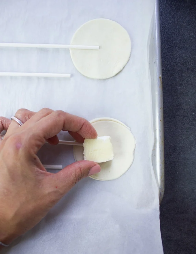 A hand putting a chunk of brie cheese at the center of the bottom crust of hand pies