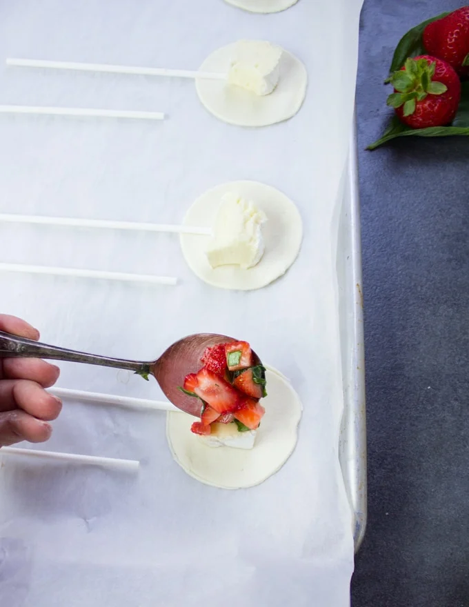 A hand adding a spoonful of strawberry mixture over the brie cheese on the bottom hand pie crust
