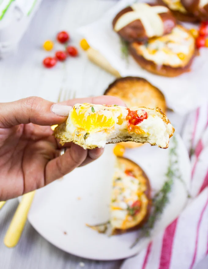 A hand holding a piece of baked egg in bread bowl bitten up shoing the inside texture of the baked eggs