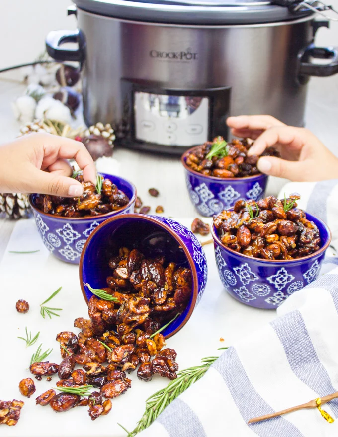 two hands grabbing the spiced mixed nuts from different bowls