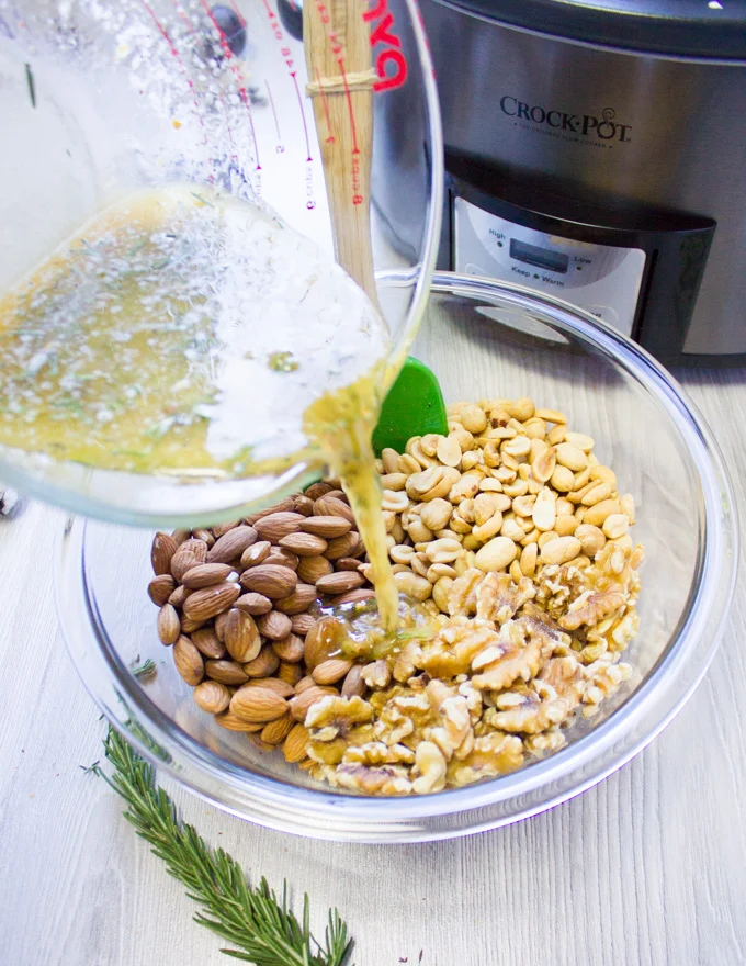 The butter and spice ingredients being poured over a bowl of mixed nuts
