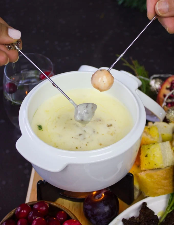 two hands sipping cheese fondue dippers in the cheese fondue pot