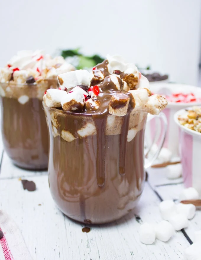 two cups of hot chocolate with toppings and chocolate sauce drizzled