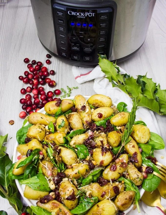 Full Plate of potato salad recipe with the crockpot and cranberries around it, and a tea towel