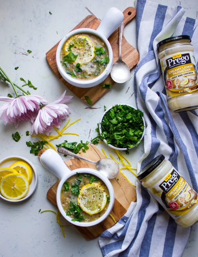 two bowls of minestrone soup surrounded by pink flowers, lemon slices, and jars of prego lemon sauce