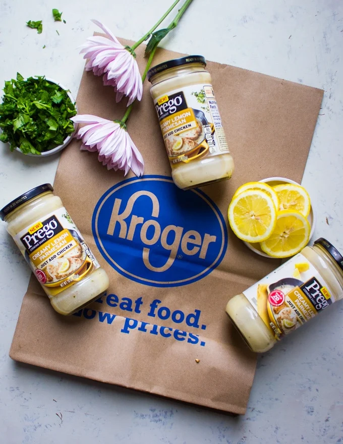 three jars of lemon cooking sauce on a bag of Kroger, some lemon slices, chopped parsley and flowers