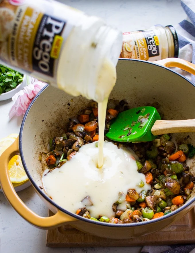 A jar of prego sauce being added to a pot of sauteed veggies to make the soup