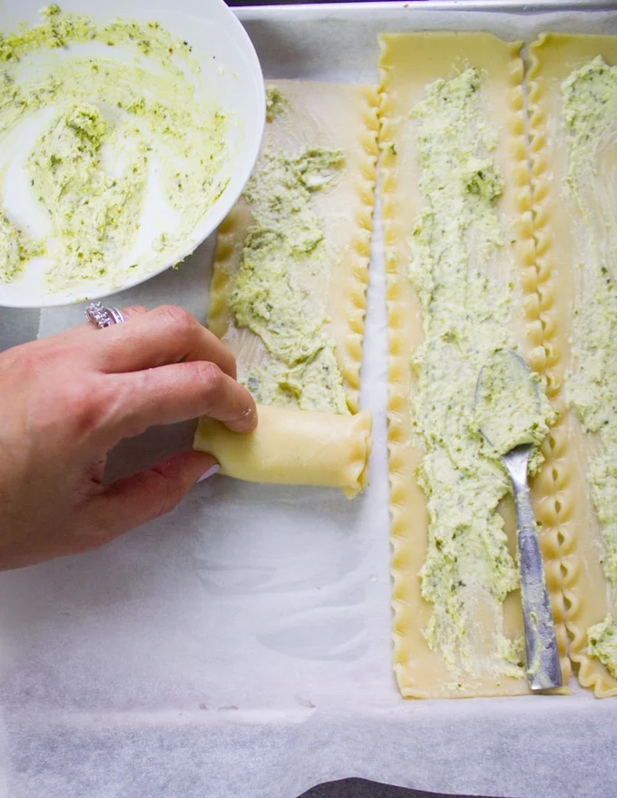 A hand rolling the lasagna sheets into a tube