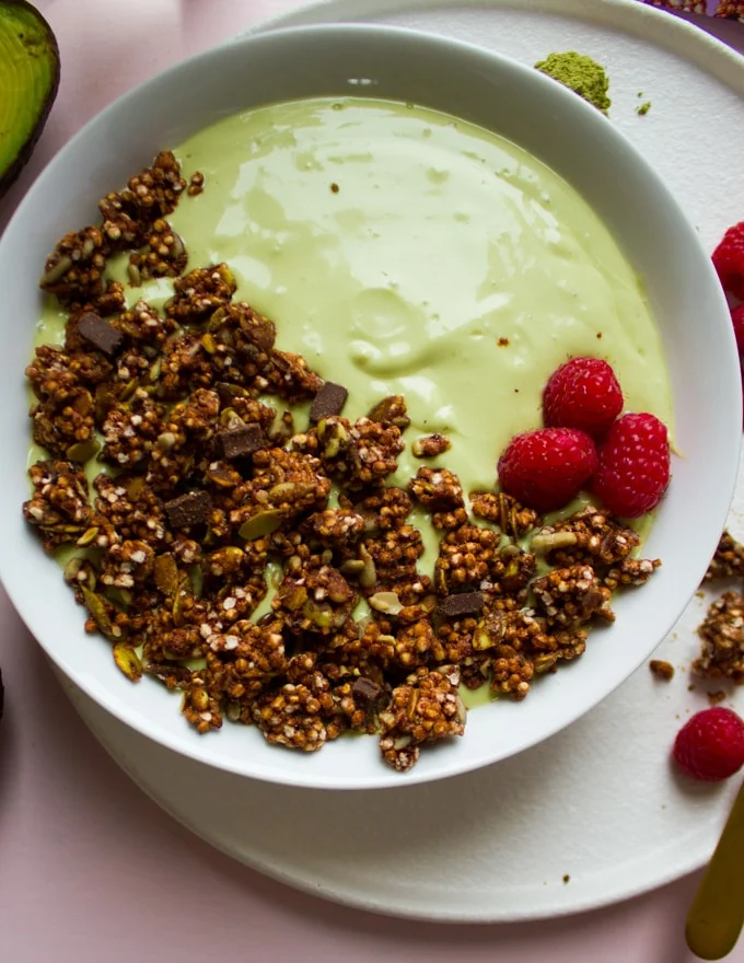 An avocado msoothie bowl with chooclate nut clusters and berries toppings
