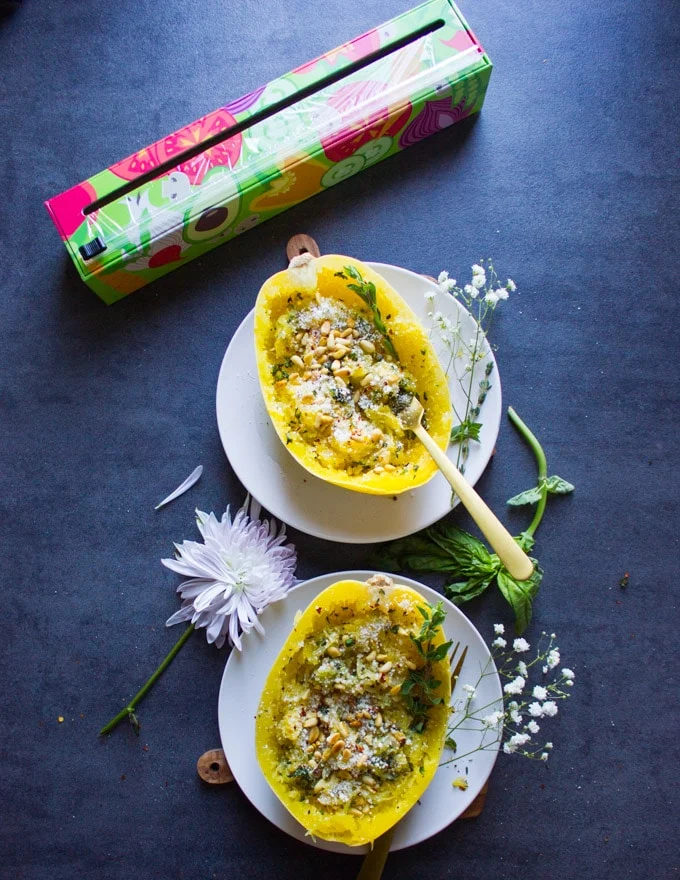 two spaghetti squash halves recipe loaded with parmesan, herbs and pine nuts on two plates and a flower in between