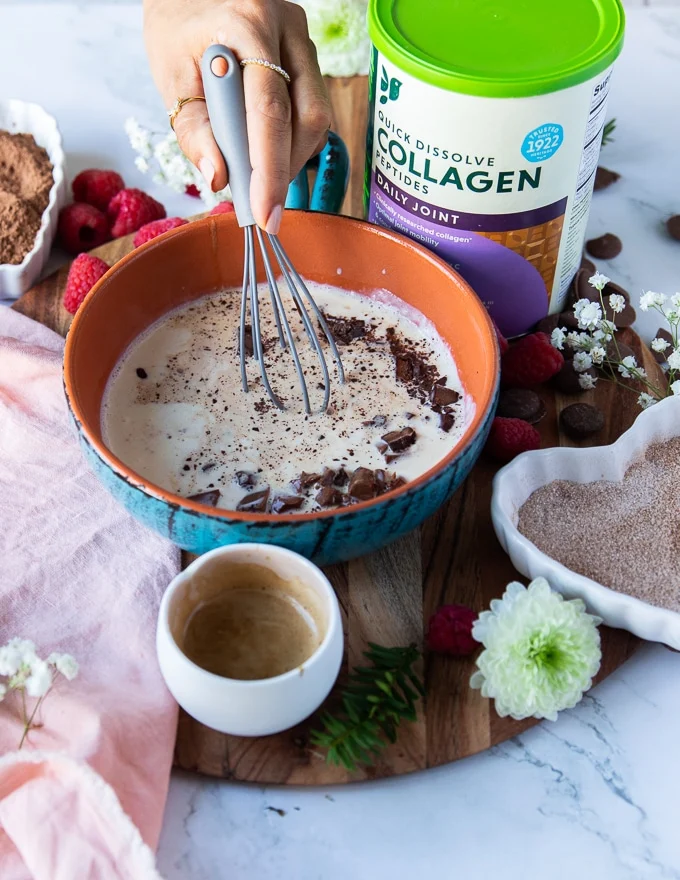 A hand holding a whisk and whisking the chocolate into the cream