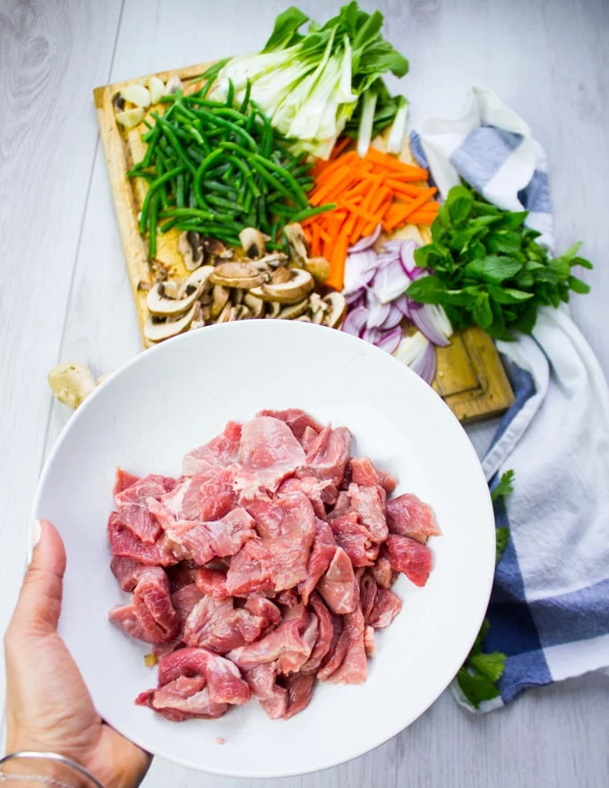 A hand holding a bowl of lamb ready to marinate with the veggies ready