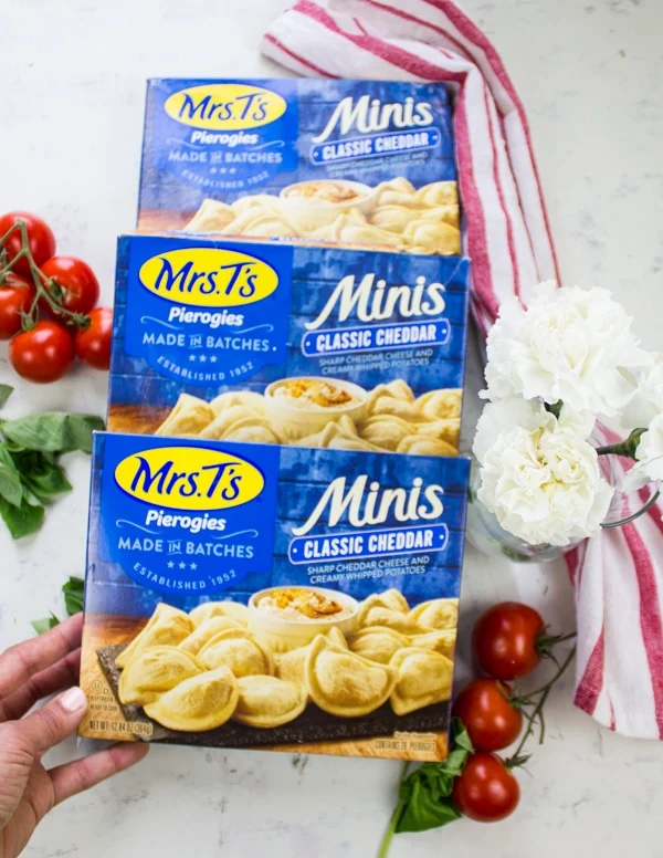 A hand holding boxes of Mrs.T's Pierogies surrounded by vine ripe tomatoes