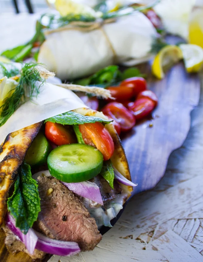 Close up of a gyro sandwich showing the lamb inside and some fresh mint, lemon juice, cucumbers and tomatoes