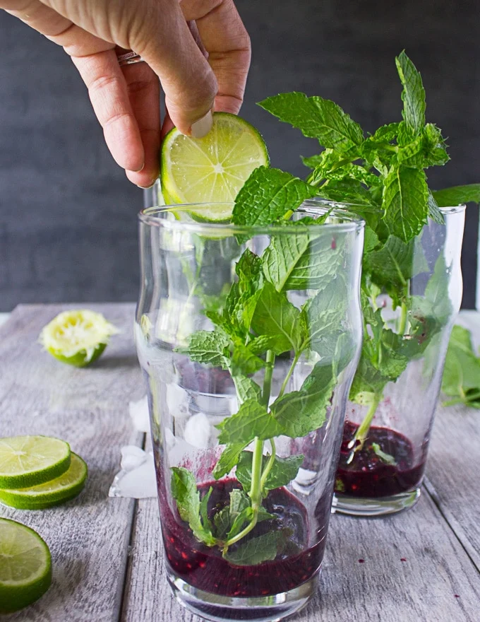 A hand adding in lime slices and mint sprigs to the cups