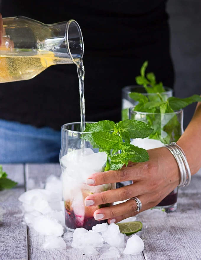 Pouring in the ginger ale/ lemon soda mixture while holding the mojitos cups with another hand to finish off the virgin mojitos recipe