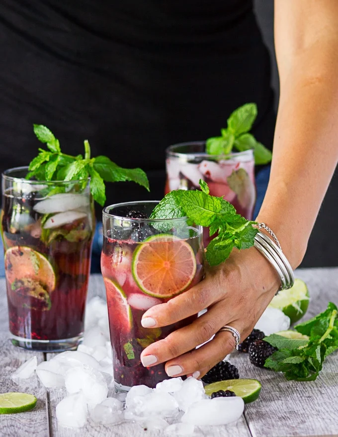 The blackberry mojito is ready to go and a hand is about to pick it up now