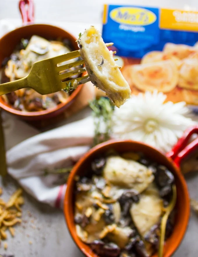 A fork holding a bitten piece of pierogies in alfredo sauce